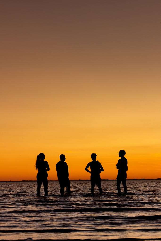 Silhouettes of four people standing in the water against a vibrant sunset in Carreras, Argentina.